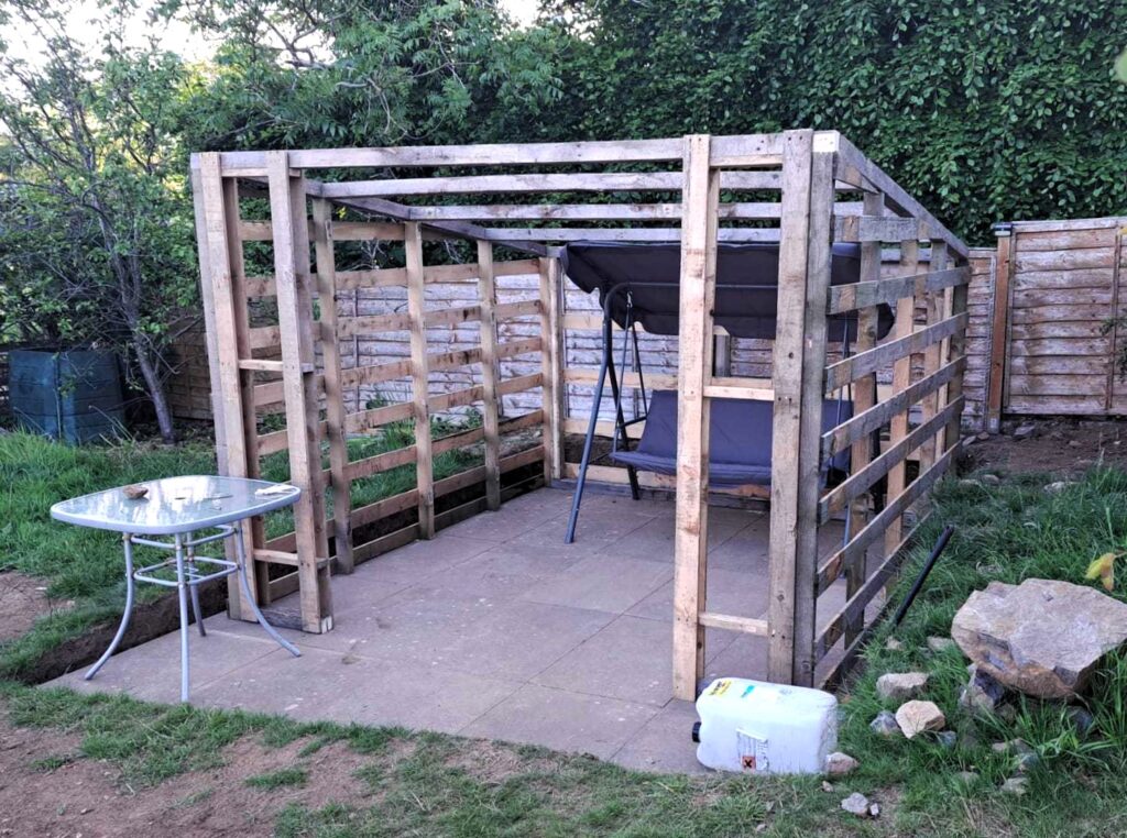 Frame of repurposed wooden pallet summer house in garden.