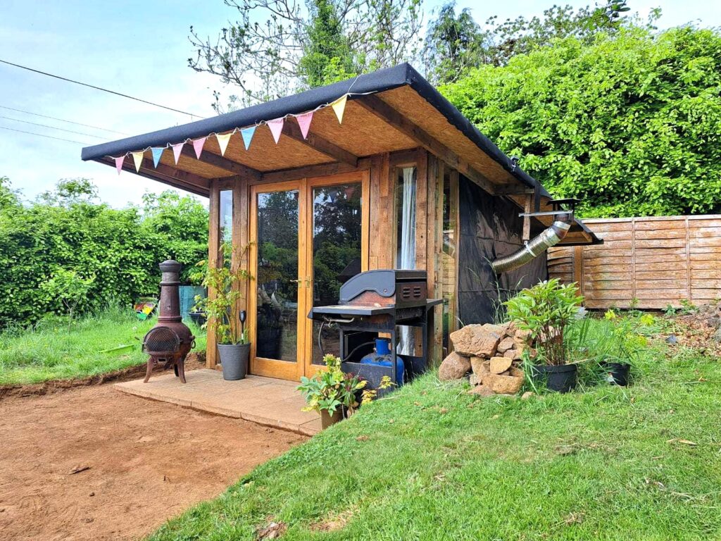 Repurposed wooden pallet summer house in a sunny garden with bunting and BBQ.